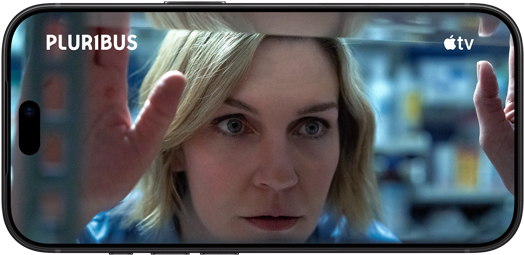 iPhone 18 Pro, mode paysage, affichant un gros plan d'une femme regardant à travers une étagère. Nom de la série : Pluribus