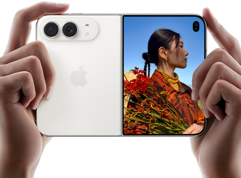 iPhone Duo, finition blanc stellaire, tenu à deux mains en position horizontale, déplié, le volet extérieur gauche présente les caméras arrière Fusion 48 MP, le volet extérieur droit présente l'écran externe affichant une personne qui se fait photographier et peut voir son propre visage pendant la prise de vue à l'aide de Duo Preview