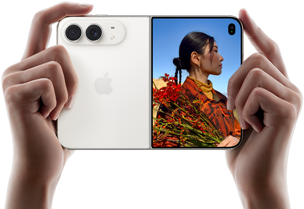 iPhone Duo, finition blanc stellaire, tenu à deux mains en position horizontale, déplié, le volet extérieur gauche présente les caméras arrière Fusion 48 MP, le volet extérieur droit présente l'écran externe affichant une personne qui se fait photographier et peut voir son propre visage pendant la prise de vue à l'aide de Duo Preview