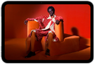 iPad mini, vue de face, écran affichant une image éclatante d'une personne portant un costume orange, assise sur une chaise orange, dans une pièce orange