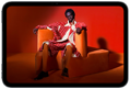 iPad mini, vue de face, écran affichant une image éclatante d'une personne portant un costume orange, assise sur une chaise orange, dans une pièce orange